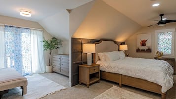 Une chambre à coucher avec un grand lit, des lampes de chevet, une table de chevet, une commode, une plante en pot et un ventilateur de plafond.
