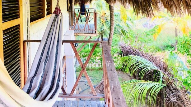 A thatched-roof veranda with a hammock and a wooden deck overlooking a lush garden.