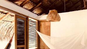 A room with a bed, a hammock, and a woven light fixture.
