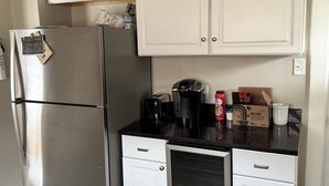 A compact kitchen with a stainless steel refrigerator, white cabinets, a built-in oven, and a coffee maker on the countertop.