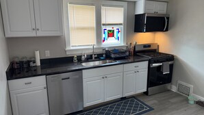 A modern kitchen with white cabinets, a black countertop, a stainless steel sink, a microwave, and a stove.