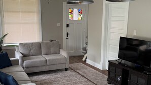 A living room with a grey sofa, a wooden dining table, and a TV on a cabinet.