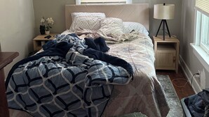 A bedroom with a bed, a nightstand, a lamp, and a window with blinds.