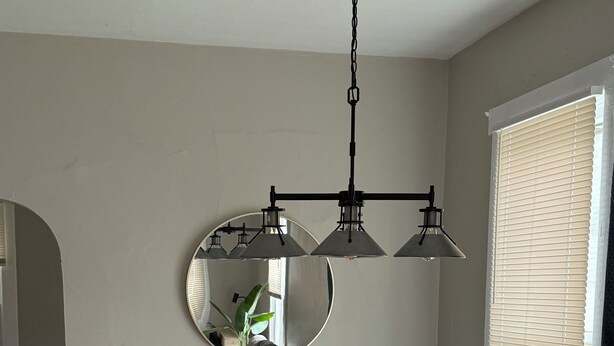A dining area with a wooden table and white chairs, a round mirror, and a ceiling light fixture.