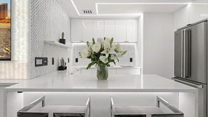Une cuisine moderne avec des meubles blancs, un îlot central doté de sièges et un réfrigérateur en acier inoxydable.