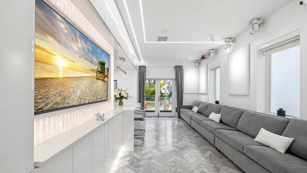 Un salon moderne avec un canapé gris, un grand écran de télévision et un parquet à motifs en chevrons.