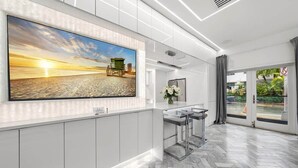 Un hall d’hôtel moderne doté d’un grand écran de télévision diffusant des images d’une plage, d’un comptoir d’accueil et offrant une vue sur l’extérieur grâce à de grandes fenêtres.