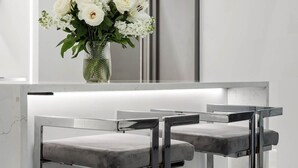Un espace bar moderne avec deux tabourets et un vase de fleurs blanches posé sur un comptoir en marbre.