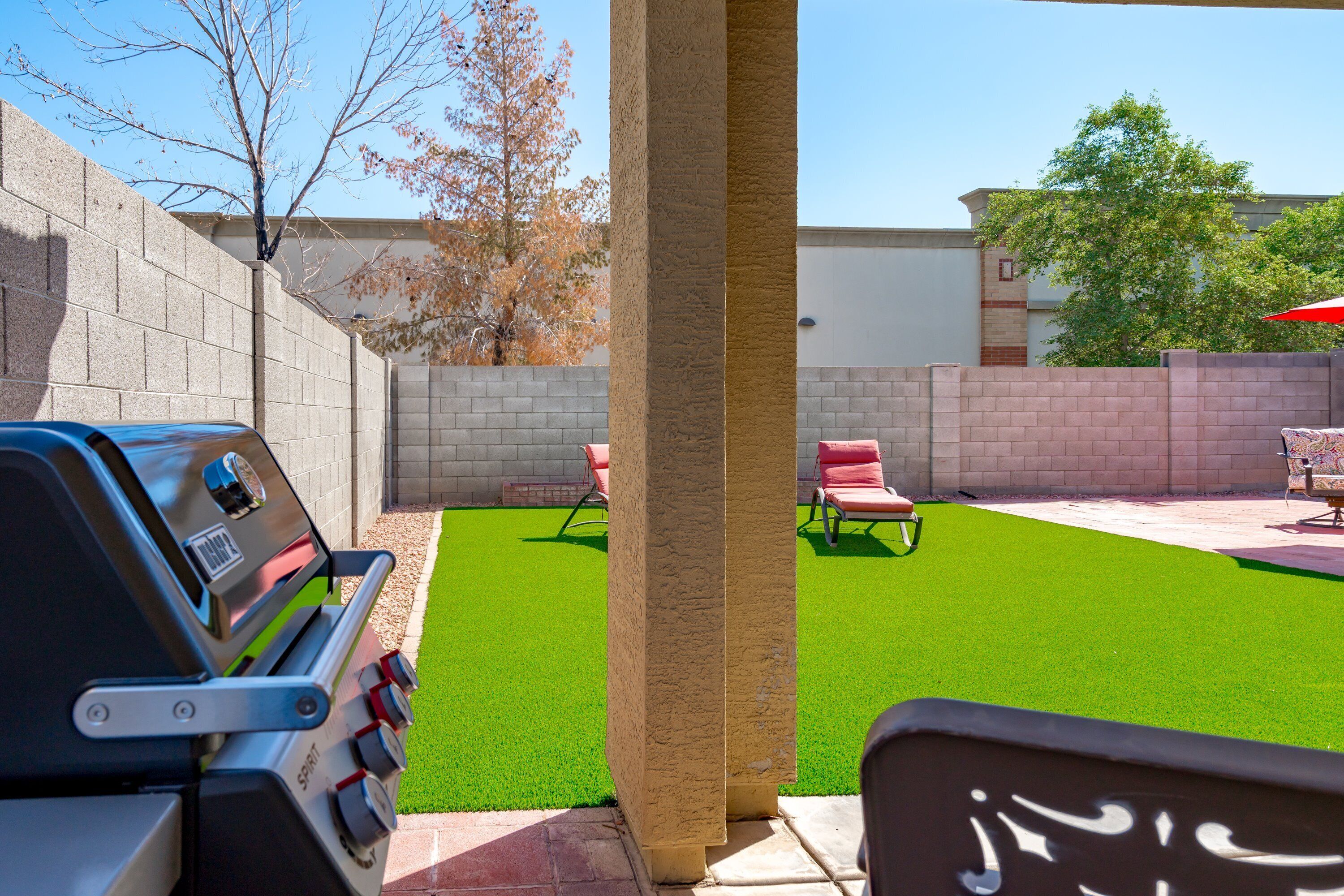 Un patio trasero con césped artificial verde, una parrilla y mobiliario de exterior.
