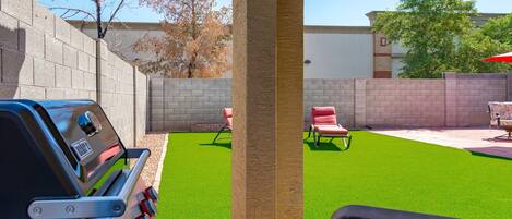 Un patio trasero con césped artificial verde, una parrilla y mobiliario de exterior.