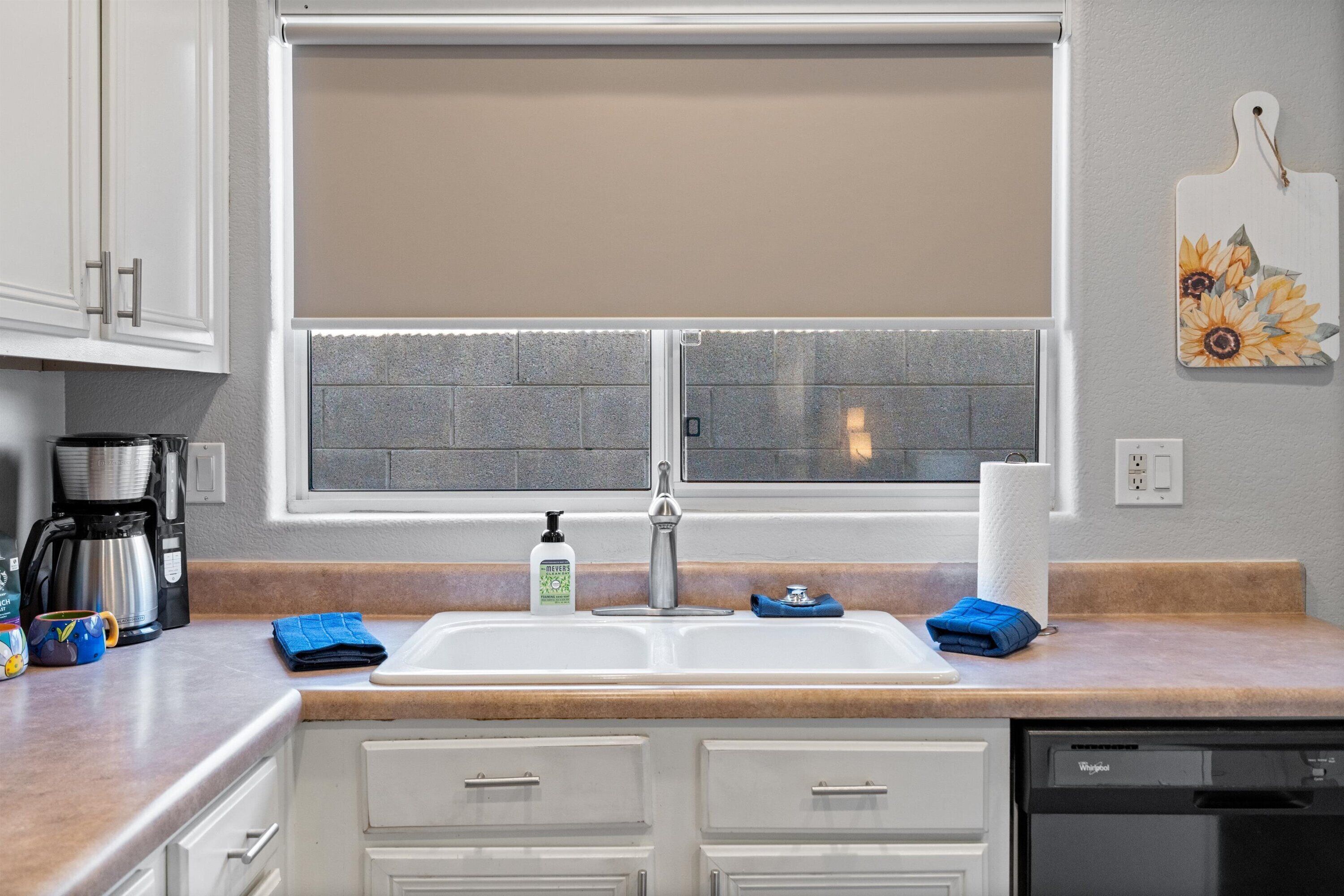 A kitchen with a double sink, white cabinets, a coffee maker, and a dish rack.