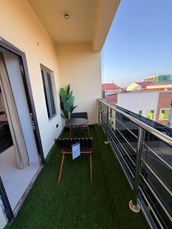A balcony with artificial grass, a small table and chairs, a potted plant, and a view of buildings.