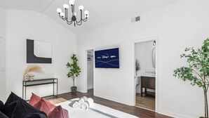 Una habitación de hotel moderna con una cama grande, un televisor mostrando servicios de streaming, un escritorio con una planta y vista al baño.