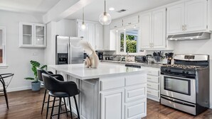 Una cocina moderna con armarios blancos, electrodomésticos de acero inoxidable y una isla central con taburetes de bar.