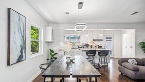 Una cocina moderna con armarios blancos, una isla central y un comedor con mesa y sillas de madera.