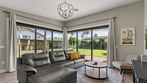 A modern living room with a sectional sofa, a round coffee table, and a view of a green landscape through large windows.