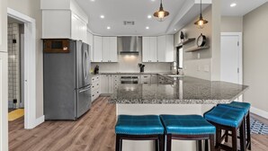 A modern kitchen with a granite island, stainless steel appliances, and blue bar stools.