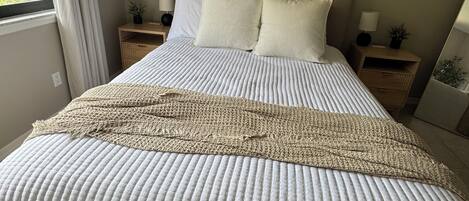 A neatly made bed with a white quilt and a beige throw blanket, two white pillows, and a wooden headboard.