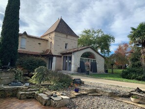 A two-story stone house with a tiled roof, a stone porch, and a garden with a gravel pathway.