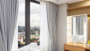 Ein Hotelzimmer mit großem Fenster, einem hölzernen Schminktisch und einem Bett mit weißer Bettwäsche.