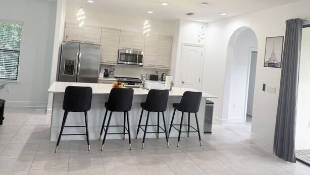 Una cocina moderna con una isla central, electrodomésticos de acero inoxidable y taburetes negros.