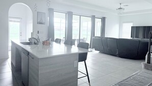 Una cocina moderna con una isla central, ventanas amplias y un rincón de estar con sofá y sillones.