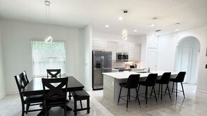 Una cocina moderna con una isla central, electrodomésticos de acero inoxidable y un comedor con mesa y sillas.