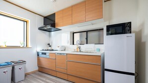 A modern kitchen with wooden cabinets, a white refrigerator, a microwave, and a dishwasher. - FUKA KAZEHANA MINBAKU OOMORIHONCHO｜11 min. direct access to Haneda Airport, private house for rent (大田区大森本町)