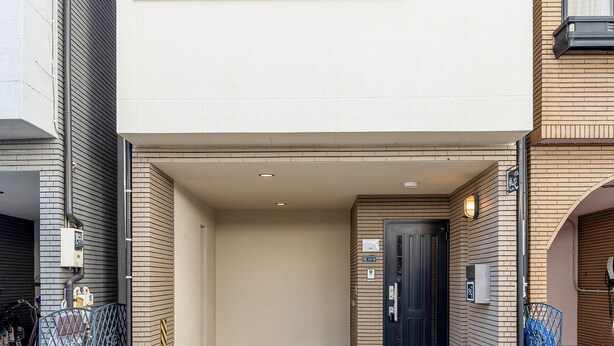 A two-story building with a flat facade, a large window on the upper floor, and a door with a sign indicating the entrance. - FUKA KAZEHANA MINBAKU OOMORIHONCHO｜11 min. direct access to Haneda Airport, private house for rent (大田区大森本町)