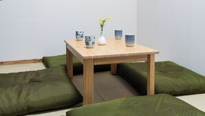 A room with a low wooden table, green cushions, a wall-mounted artwork, and a vase with flowers. - FUKA KAZEHANA MINBAKU OOMORIHONCHO｜11 min. direct access to Haneda Airport, private house for rent (大田区大森本町)