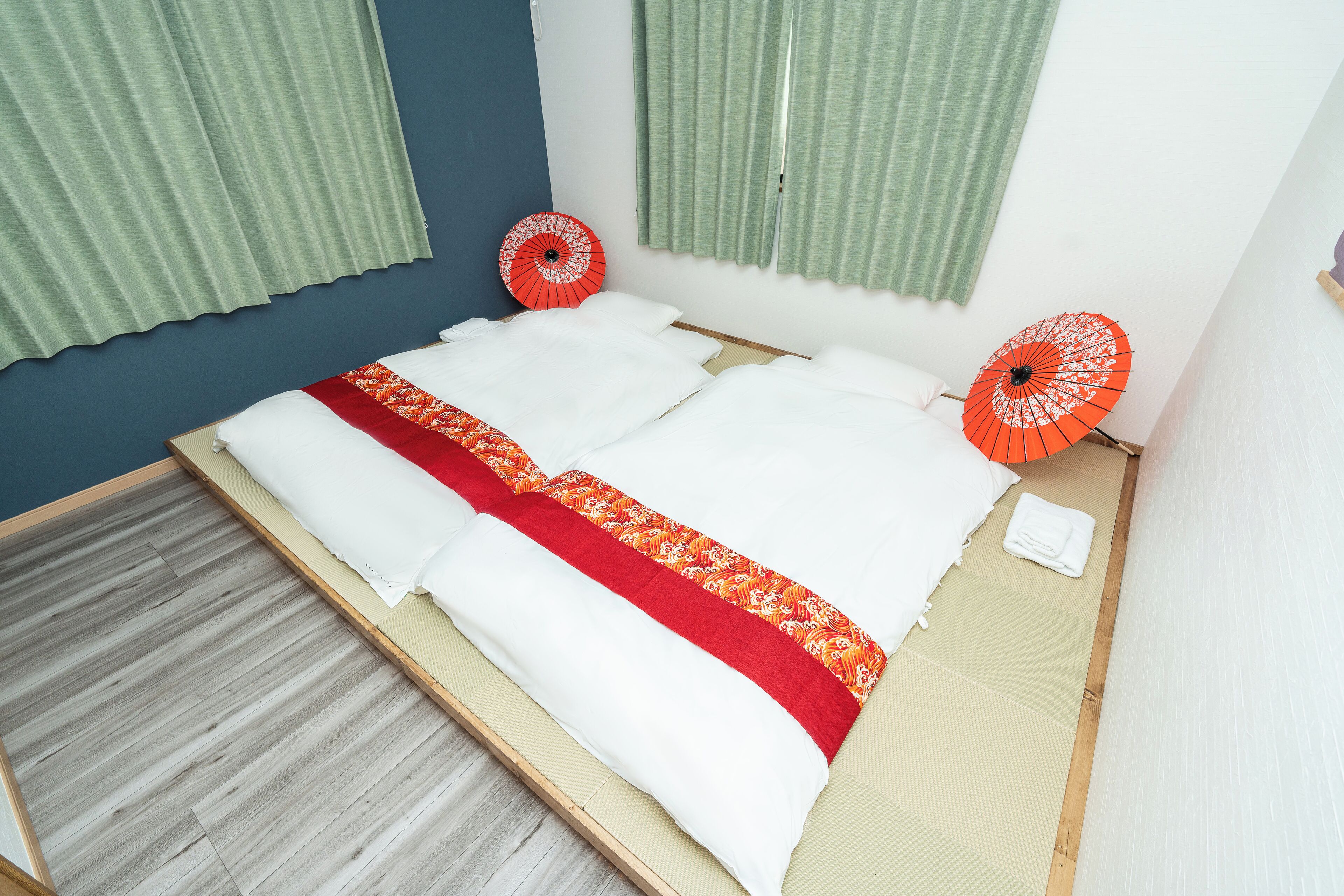 A bed with a white and red bedspread, two red umbrellas, and a wooden floor.
