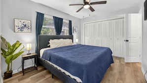 Ein Schlafzimmer mit Bett, Deckenventilator, Nachttisch, Lampe, Topfpflanze und Kleiderschrank.