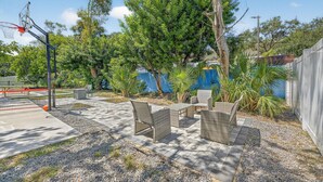 Ein möblierter Patio-Bereich im Freien mit Korbmöbeln, einem Basketballkorb und einer blauen Wand im Hintergrund.