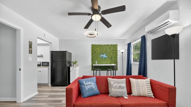 Ein modernes Wohnzimmer mit einem roten Sofa, einem Deckenventilator, einem schwarzen Kühlschrank und einer grünen Wanddekoration.