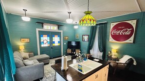 Un salon chaleureux aux murs de couleur turquoise, avec un canapé gris, une table basse et un coin cuisine comprenant un évier et un plan de travail.