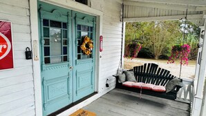Un porche avec une porte de couleur turquoise, un banc et un panier à fleurs suspendu.