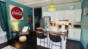 Une cuisine compacte dotée d’un îlot central, de meubles blancs, d’un réfrigérateur et d’un four à micro-ondes.