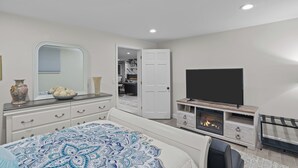 A bedroom with a bed, dresser, mirror, wardrobe, TV, and fireplace. - Autumn Estate (Westport)