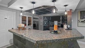 A kitchen with granite countertops, hanging pendant lights, and a central island with a bar setup. - Autumn Estate (Westport)