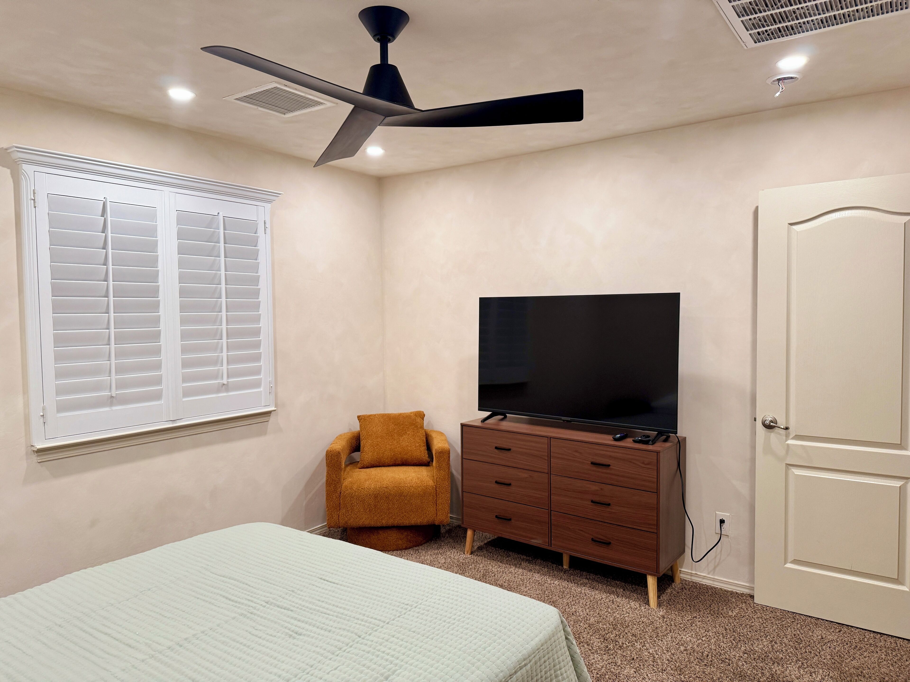 A bedroom with a bed, a TV on a dresser, a chair, and a door.