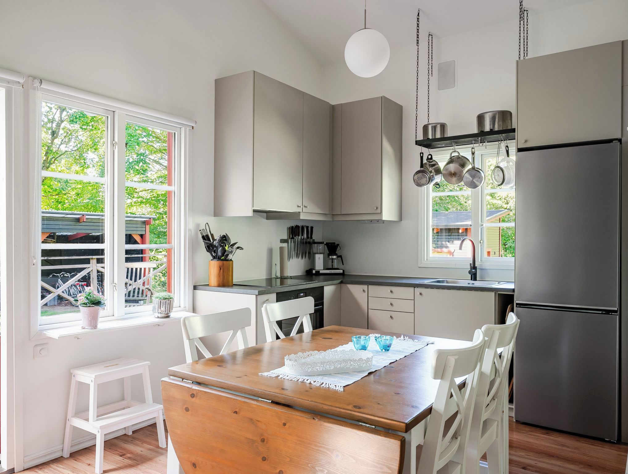Une cuisine moderne avec des meubles blancs, une table à manger en bois et un réfrigérateur en acier inoxydable.