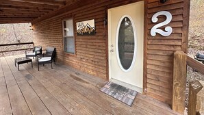 En træhytte med terrasse, en dør med nummer 2, et skilt med teksten 'Let's Explore' og en velkomst måtte.