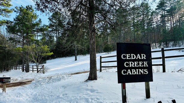 Skilt for Cedar Creek Cabins, et sneklædt landskab og et træhegn i baggrunden.