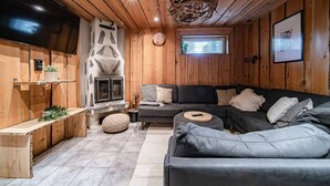 A cozy cabin interior with a fireplace, wooden walls, a sofa, and a television. - Jukola Juhani by Aavalevi Holidays (Levi)