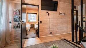 A wooden-paneled room with two beds, a TV mounted on the wall, and a small window. - Jukola Juhani by Aavalevi Holidays (Levi)