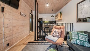 A modern interior with a wooden wall, a black metal staircase, a sofa, and a dining area. - Jukola Juhani by Aavalevi Holidays (Levi)