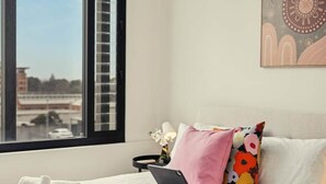 Een moderne slaapkamer met een groot raam, een bed met witte lakens, een laptop op het bed en een decoratief wandobject.