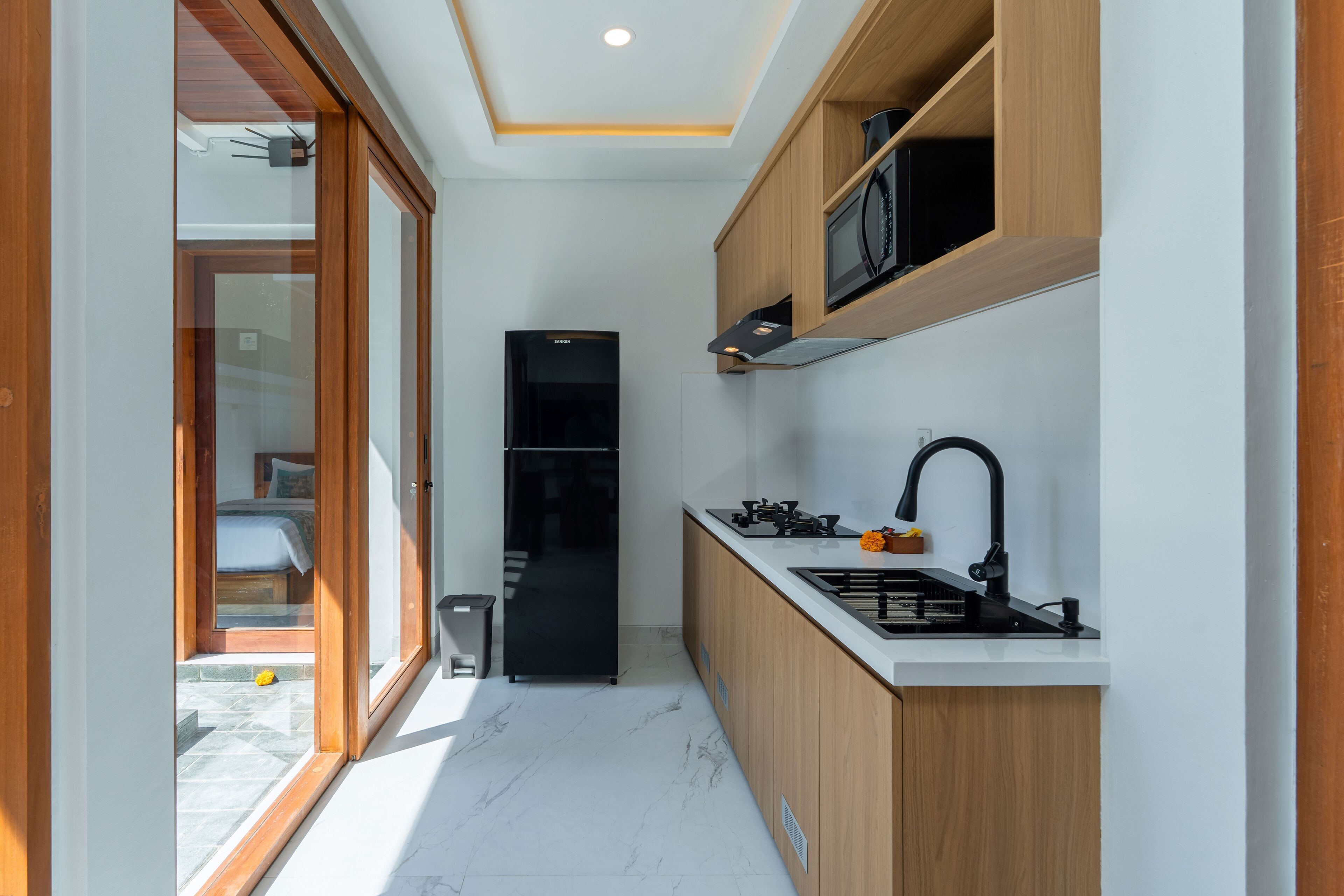 A compact kitchen with a black refrigerator, wooden cabinets, a white countertop, and a black sink.