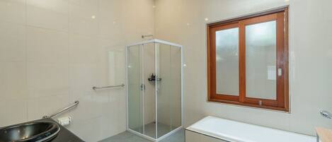 A modern bathroom with a glass shower enclosure, a bathtub, and a toilet with a bidet attachment.