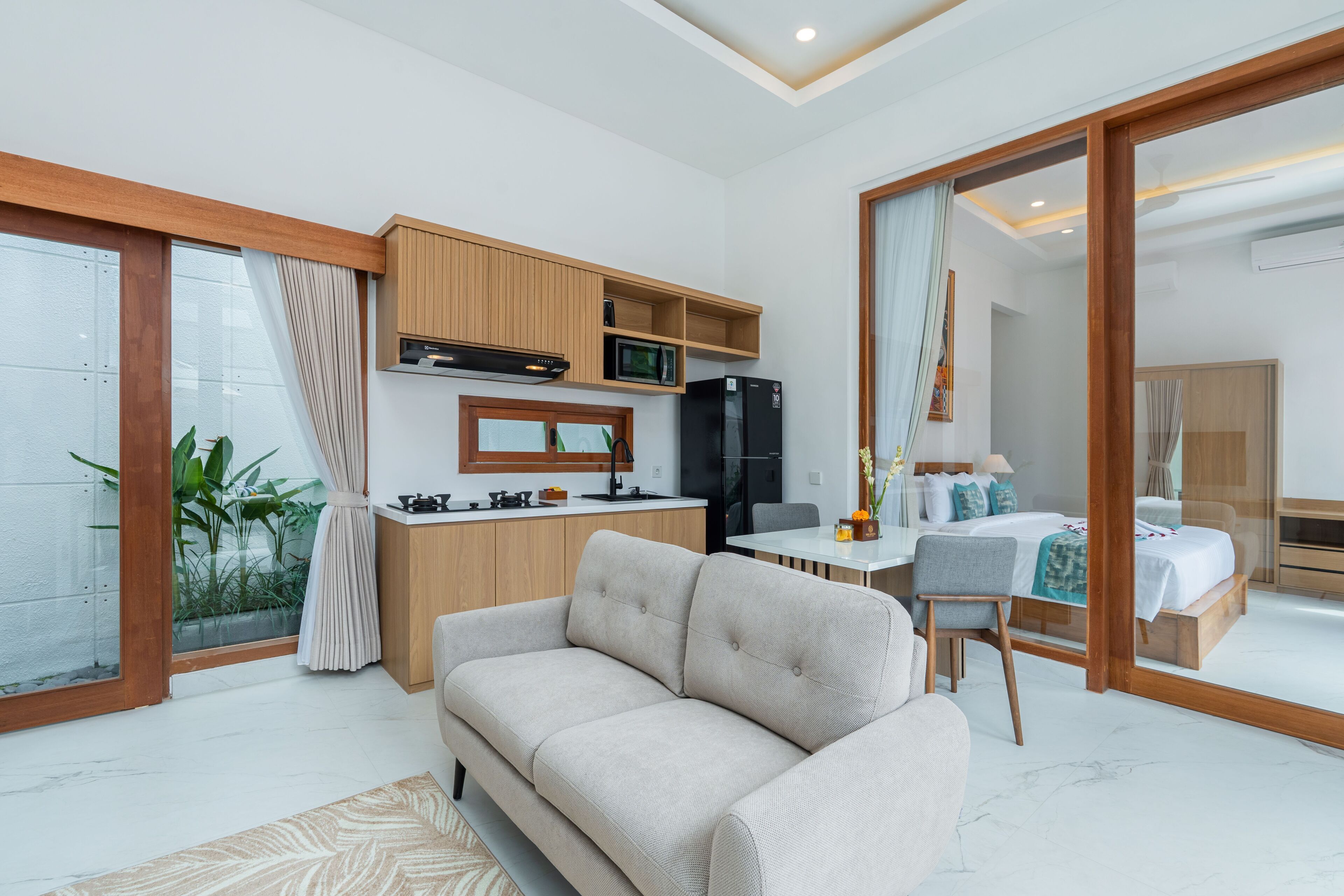 A modern living room with a sofa, a dining table, a kitchen area with a microwave and refrigerator, and a bedroom with a bed and a nightstand.
